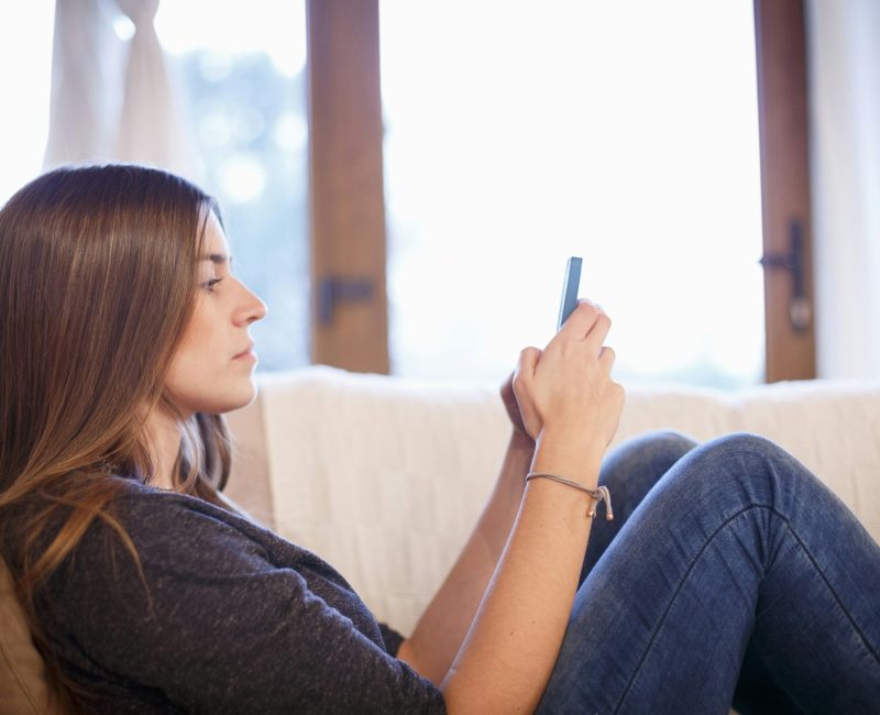 Young woman using cellular phone on sofa